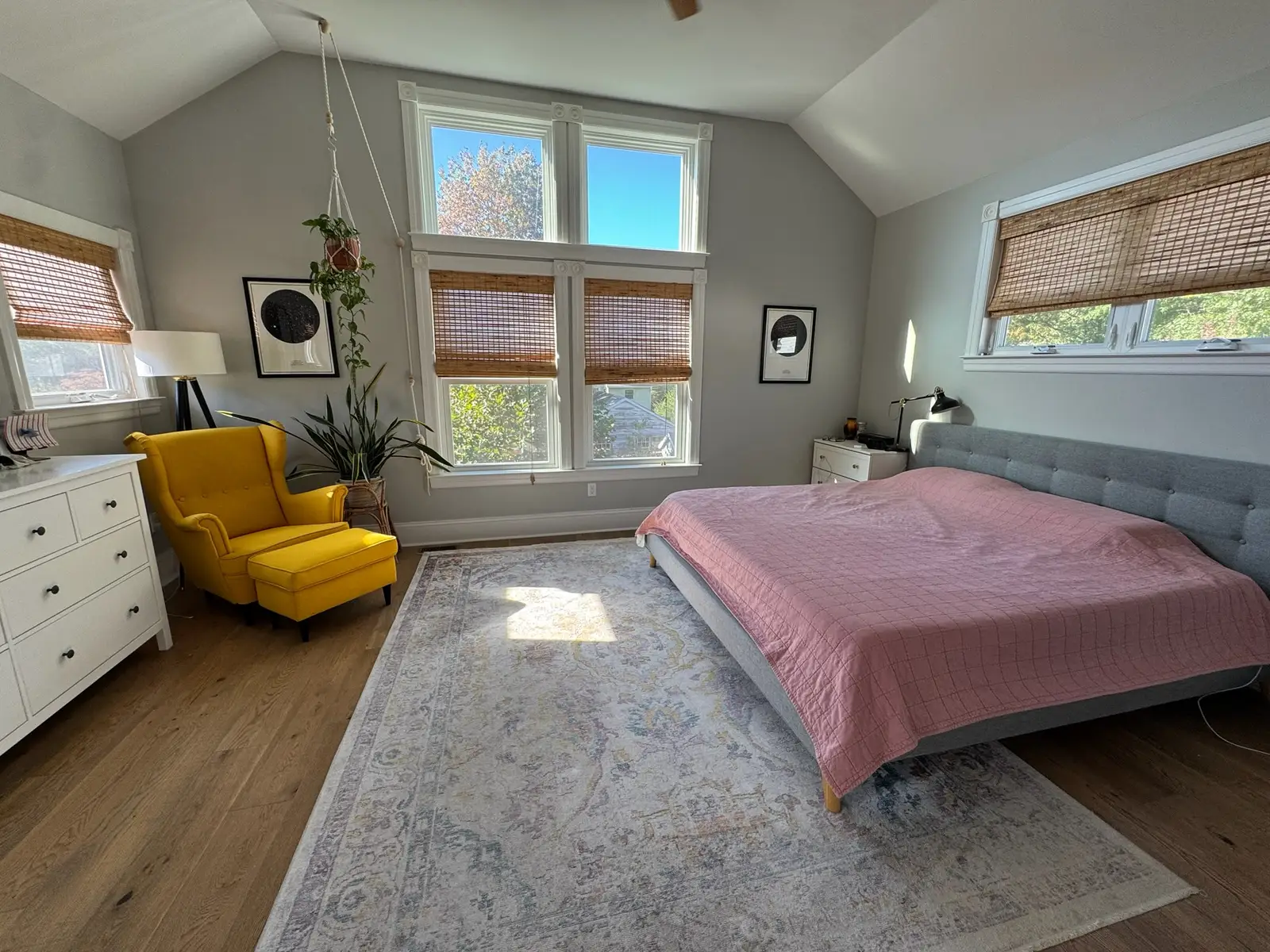 Master bedroom on the addition's second floor with a vaulted ceiling, a bed under a wide window, and a tall four-pane window on the gable wall