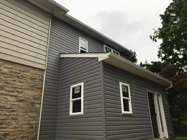 Finished outside of the Glenside addition in gray siding with white-trimmed windows, joined to the stone and siding of the original house