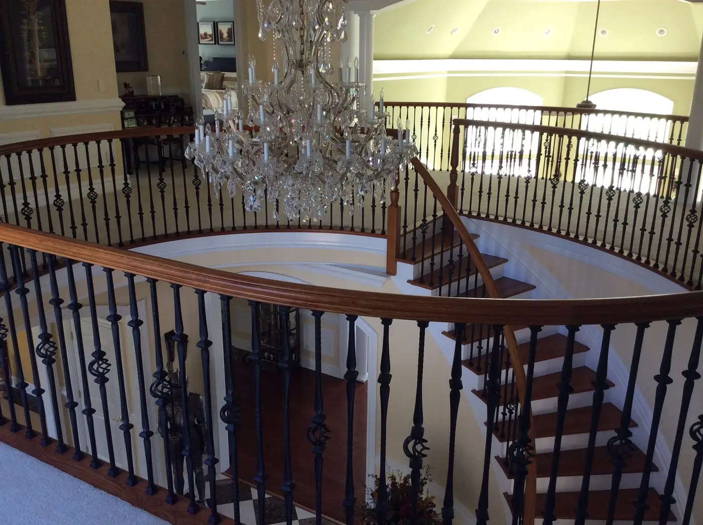 View from the balcony over the curved iron railing and crystal chandelier, looking down into the foyer