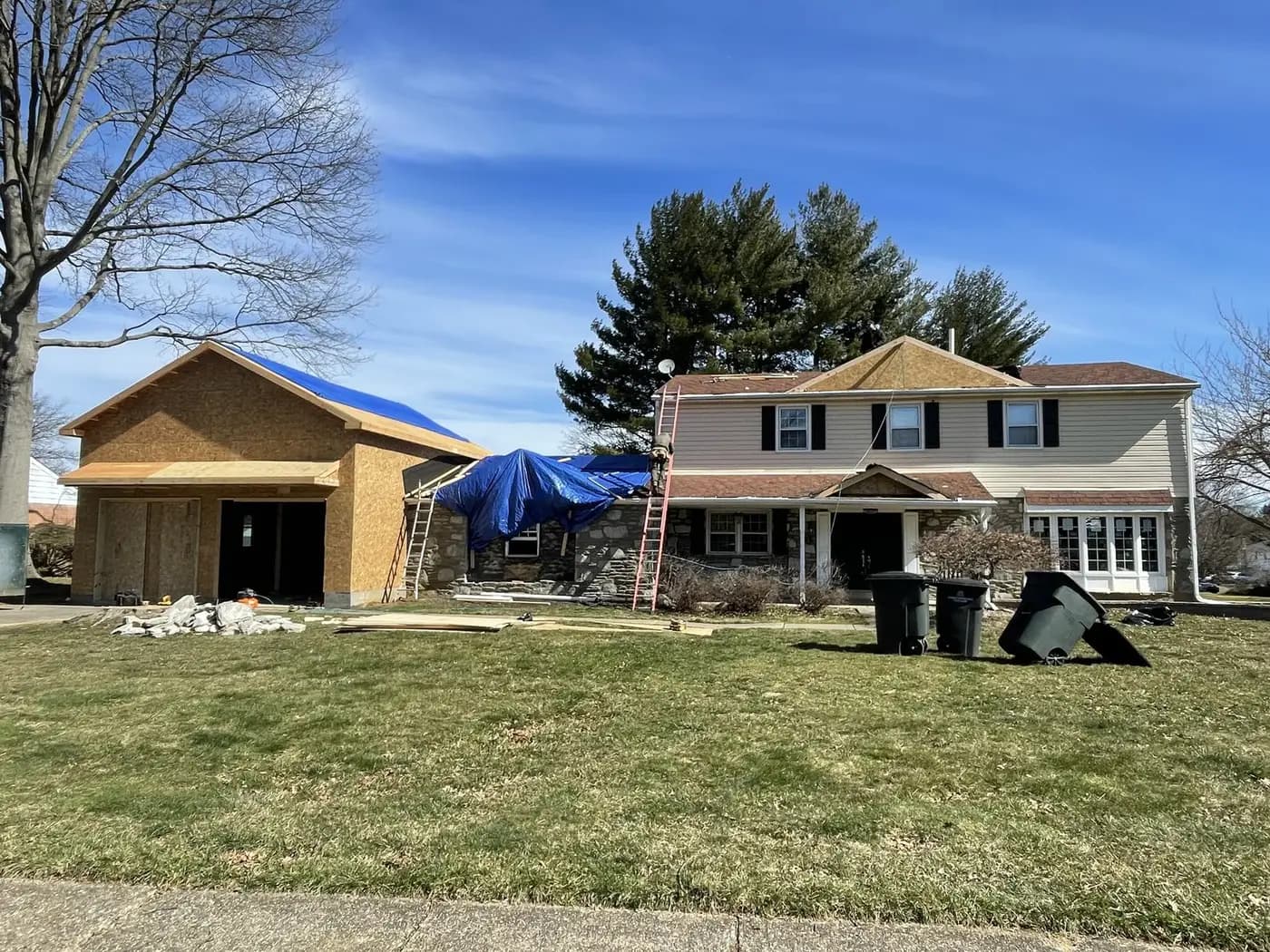 The addition sheathed and wrapped beside the house, materials on the lawn