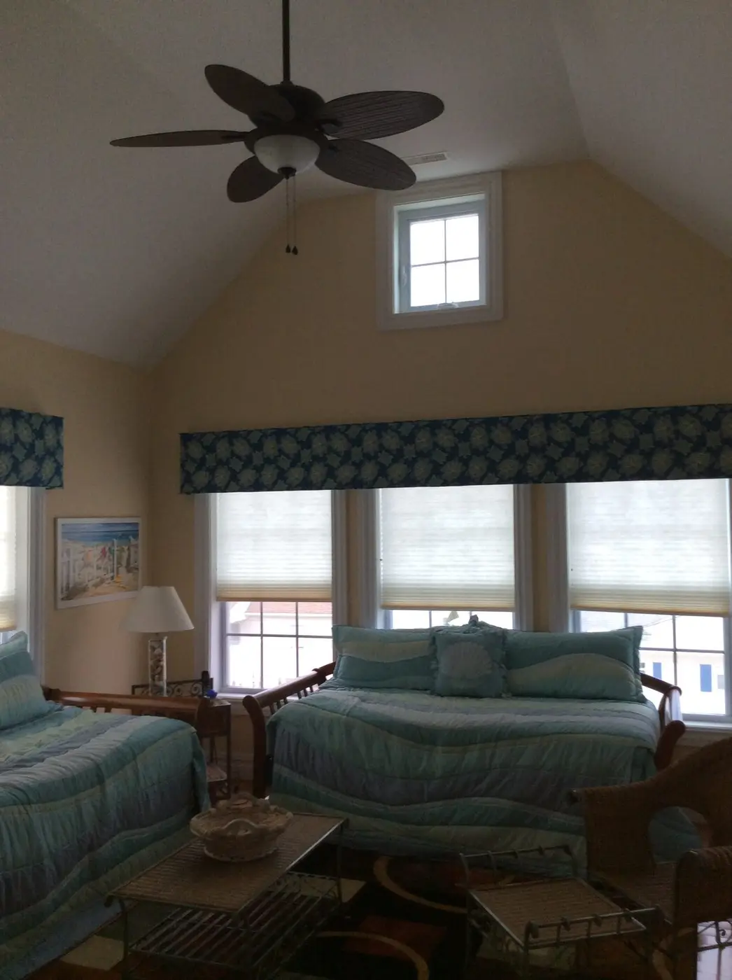 Bedroom with a vaulted ceiling and ceiling fan, three windows under a patterned valance, and two beds