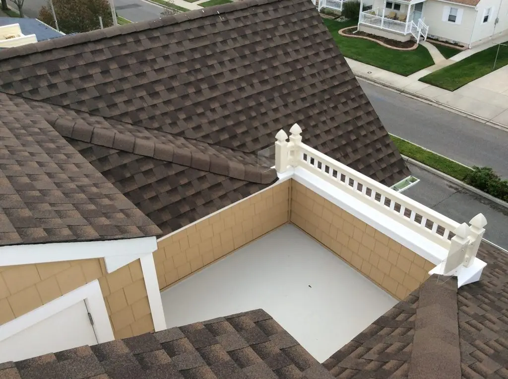 View across the shingled roof to the small rooftop deck with white railing and the street below