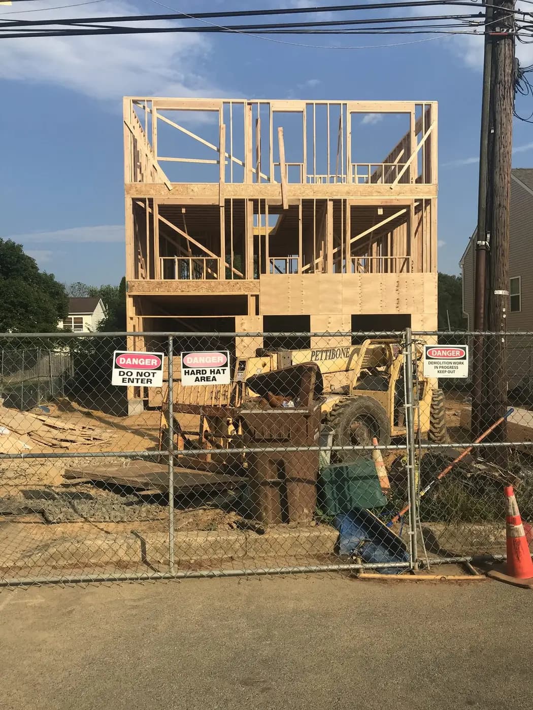 Three stories of wall framing standing behind a chain-link construction fence, with a lift parked in front