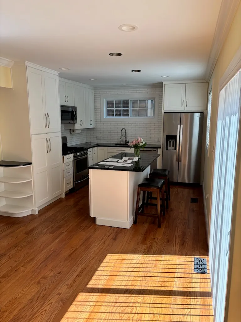 Kitchen in the Conshohocken house: white cabinets, a subway tile backsplash, stainless appliances, and a dark-topped island with two stools on hardwood floors